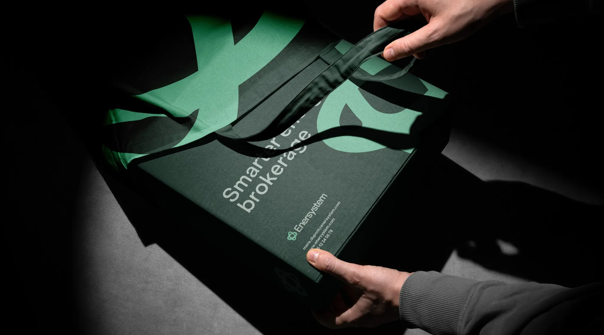 Hands holding an Enersystem folder with the green Enersystem symbol, brand identity by Logomint