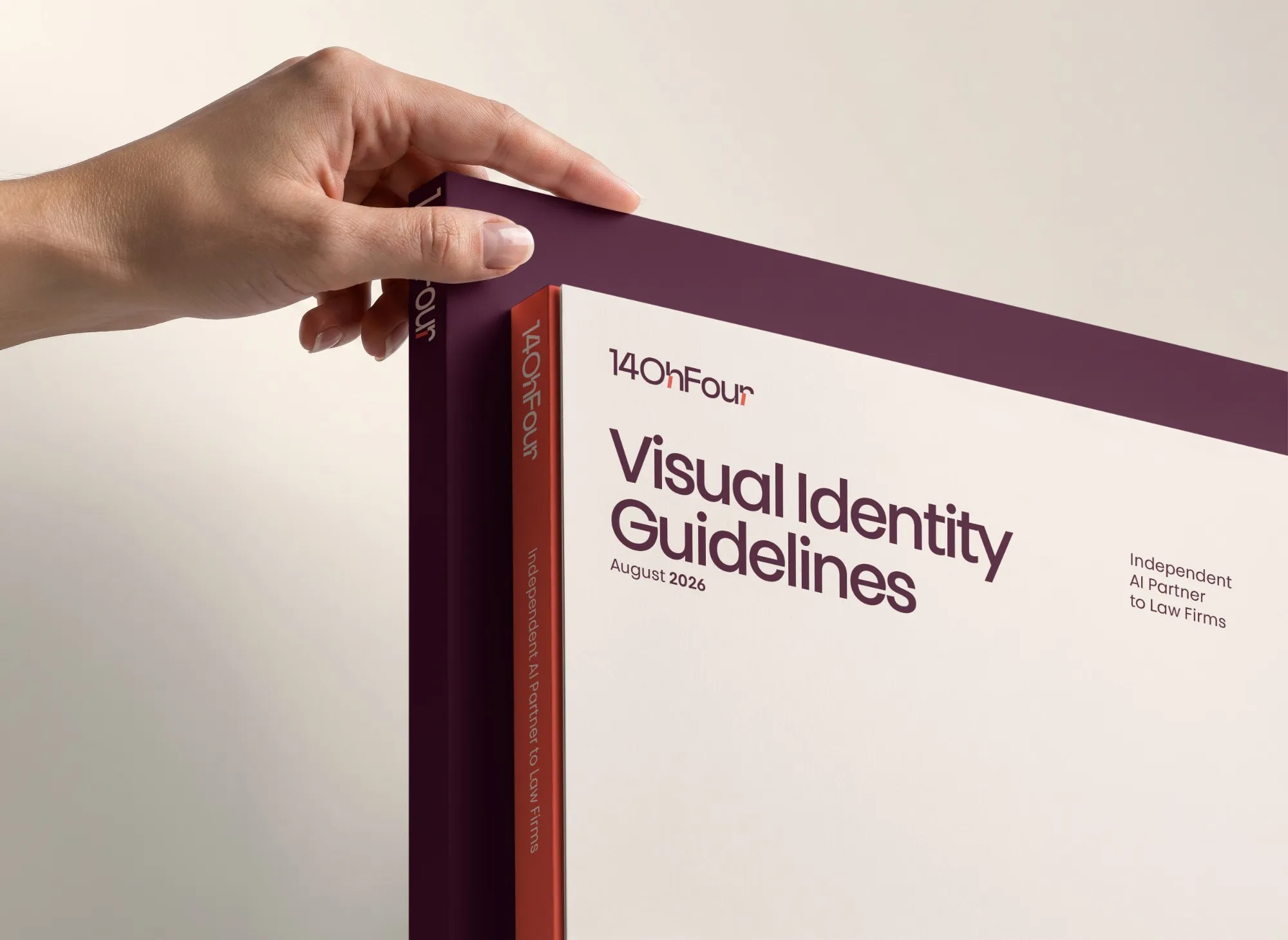 Hand opening the 14OhFour Visual Identity Guidelines book with a burgundy cover