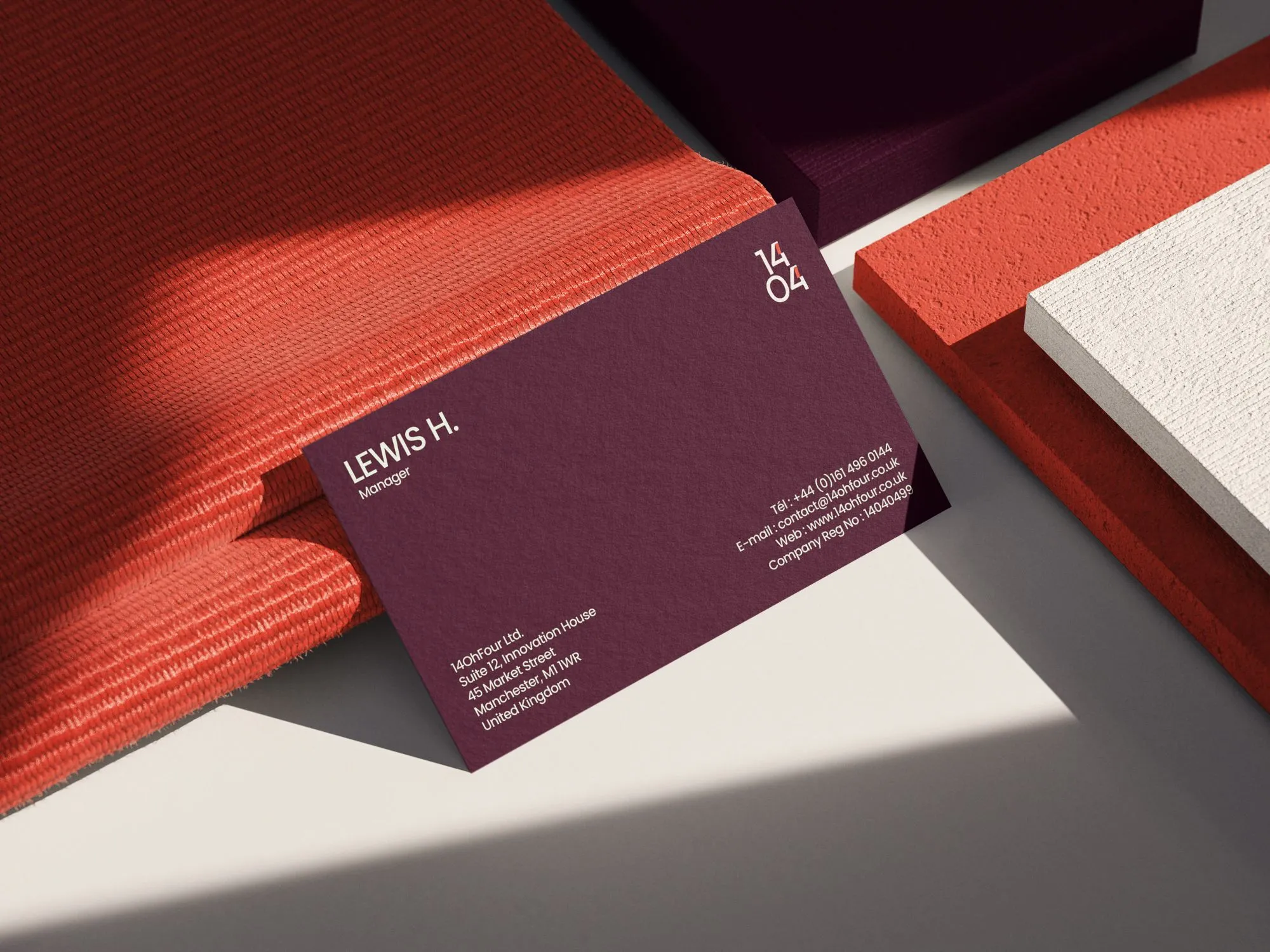 Burgundy 14OhFour business card with the compact 14/04 mark, resting on coral fabric